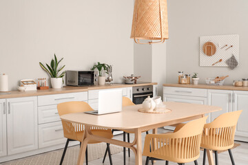 Interior of modern kitchen with white counters, dining table, laptop, chairs and lamp