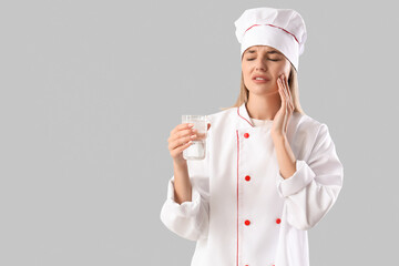 Young female chef with cooking pot suffering from tooth ache on grey background