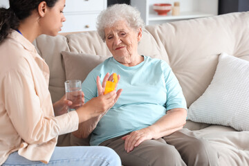 Elderly woman refusing pills from young African-American female medical worker in nursing home