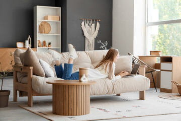 Young woman with laptop lying on sofa in living room