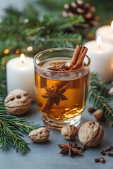 Glass of mulled cider with cinnamon star anise walnuts and candles.