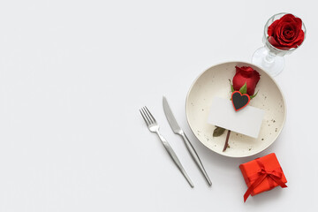 Beautiful table setting with blank card, gift box and red roses on grey background. Valentine's Day celebration