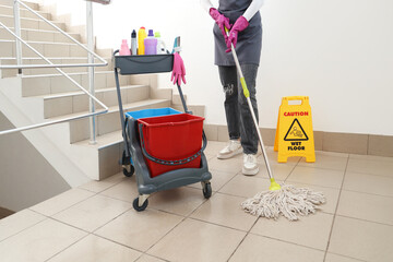 Female janitor with trolley of cleaning supplies mopping floor in stairway