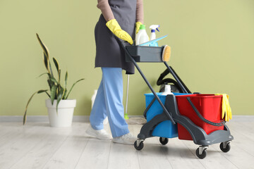 Female janitor with trolley of cleaning supplies near green wall