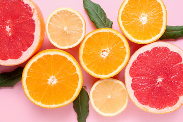 Different cut citrus fruits with leaves on pink background