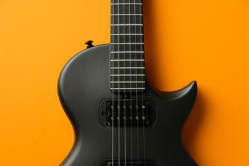 Obraz premium Close-up of a black electric guitar against a vibrant orange background