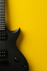 Close-up of a black electric guitar on a bright yellow background