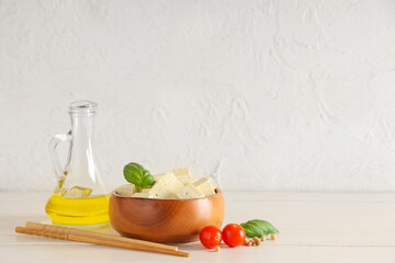 Bowl with pieces of tofu cheese on white wooden background