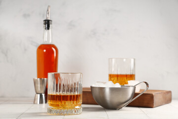 Glass of rum and bowl of ice cubes on table against blurred background. Closeup