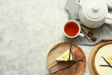 Wooden plate of sweet cheesecake slice with vanilla flower and cup of tea on grey background
