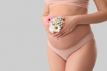Young pregnant woman in panties with flowers on light background, closeup