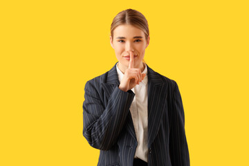 Young businesswoman showing silence gesture on yellow background