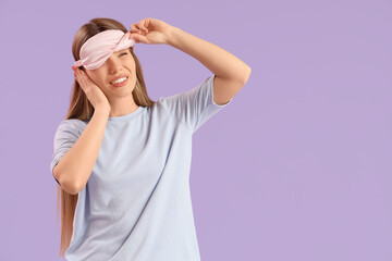 Young woman with sleeping mask suffering from loud noise on lilac background