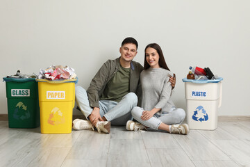 Young couple with sorted rubbish in garbage bin sitting near white wall. Global Recycling Day