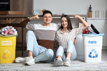 Young couple with sorted rubbish in garbage bins showing muscles at home. Global Recycling Day