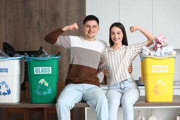 Young couple with sorted rubbish in garbage bins showing muscles at home. Global Recycling Day