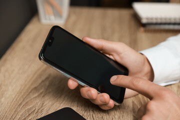 Man using smartphone with blank screen at wooden table, closeup