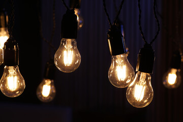Glowing light bulbs hanging indoors, closeup view