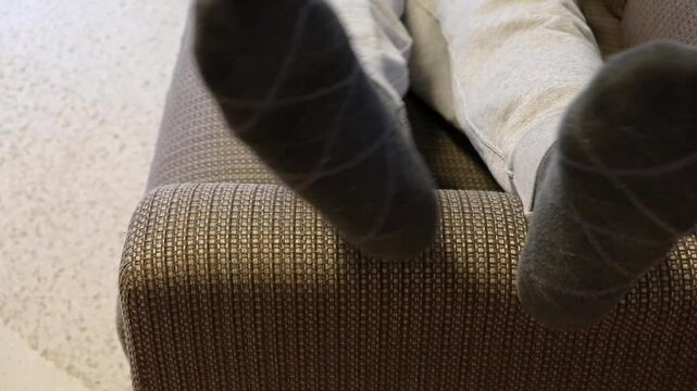 ソファーの肘掛けに足をのせて横たわる人物