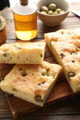 Pieces of delicious focaccia bread with olives, thyme, oil and salt on wooden table, closeup
