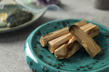 Smoldering palo santo stick and gemstone on light grey table, closeup