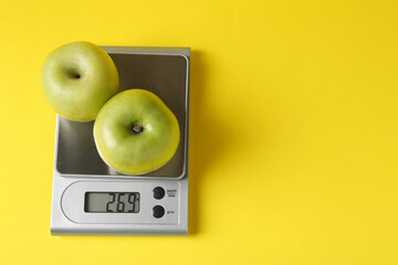 Electronic kitchen scale with apples on yellow background, top view. Space for text