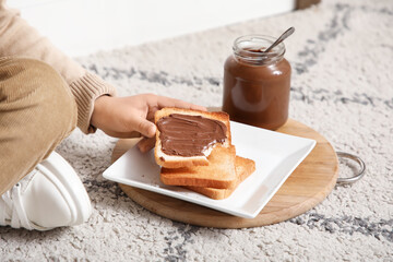 Little boy with bitten toast and jar of sweet chocolate paste in kitchen, closeup