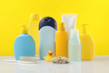 Baby cosmetic products and bath accessories on table against yellow background