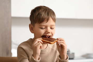 Cute little boy with chocolate paste on his face eating sweet toast in kitchen