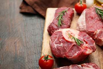 Pieces of raw beef, rosemary and tomatoes on wooden table, closeup. Space for text