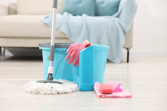 String mop and bucket with cleaning supplies on wooden floor indoors