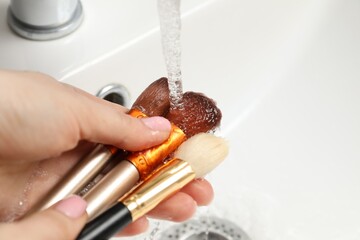 Woman washing makeup brush under stream of water in sink, closeup