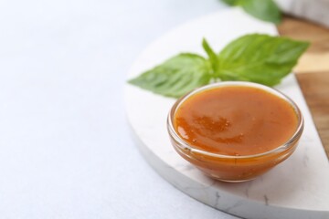 Tasty curry sauce in glass bowl and basil on white table, closeup. Space for text
