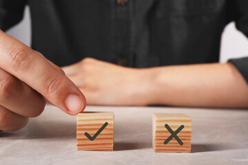 Approved. Man choosing cube with check mark instead of other one with cross at table, closeup