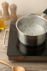 Saucepan with boiling water and stove on wooden table against white background