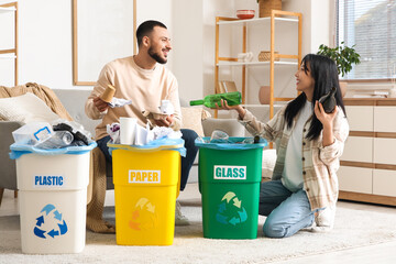 Young couple sorting rubbish in garbage bins at home. Global Recycling Day