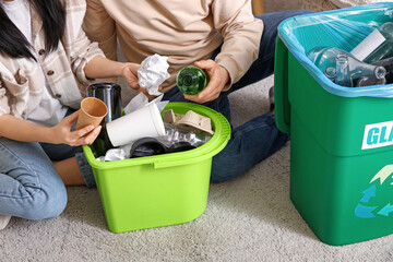 Young couple sorting rubbish in garbage bins at home, closeup. Global Recycling Day