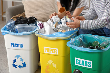 Young couple sorting rubbish in garbage bins at home, closeup. Global Recycling Day