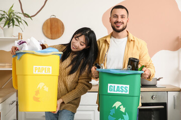 Young couple with sorted rubbish in garbage bins at home. Global Recycling Day