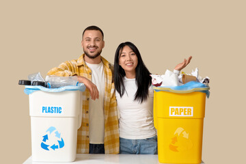 Young couple with sorted rubbish in garbage bins on beige background. Global Recycling Day