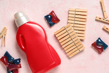 Wooden clothespins with laundry detergent and gel capsules on grunge pink background