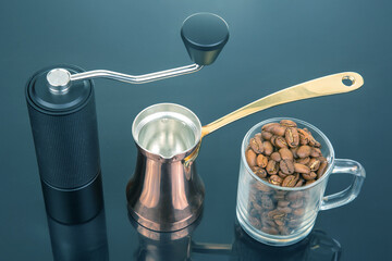 A black manual coffee grinder with a metallic handle, a copper cezve with a gold handle, and a...