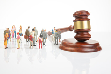 A group of miniature figurines representing diverse people stands before a large wooden gavel on a...