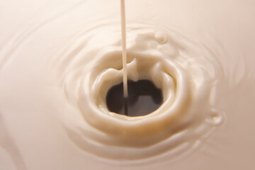 A close-up of milk splashing into a white liquid, creating ripples and a mesmerizing vortex....