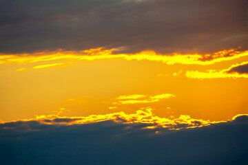 Scenic sunset with dramatic cloud formations painted in shades of orange, yellow, and deep blue. The play of light and shadow creates a mesmerizing natural composition.