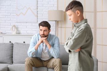 Young father and his little son thinking after squabbling at home