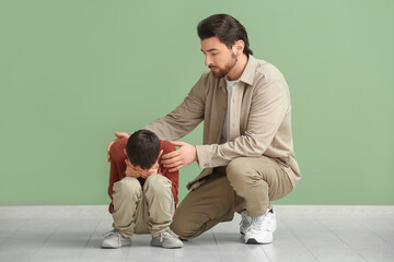 Young father trying to calm his sad little son after squabbling on green background