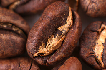 Close-up of a single roasted coffee bean, split open, revealing its inner texture amidst a pile of beans. Perfect for food photography or coffee blogs.