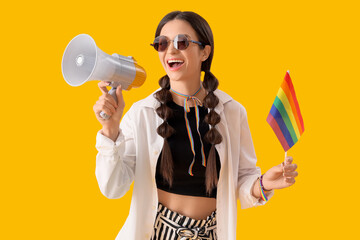 Beautiful young woman with rainbow flag and loudspeaker on yellow background. LGBT concept