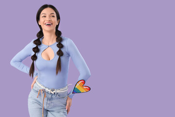 Beautiful young woman with rainbow heart on lilac background. LGBT concept